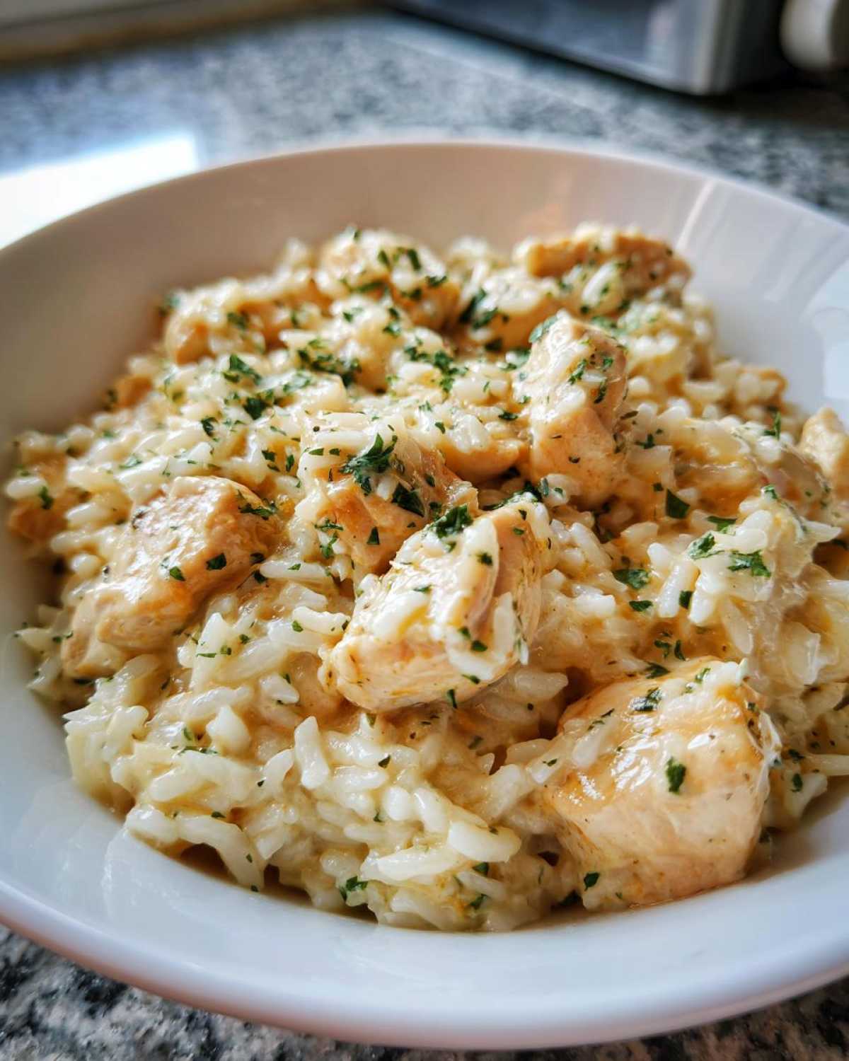 Close-up of creamy Garlic Butter Chicken and Rice dinner topped with fresh parsley in a white bowl.