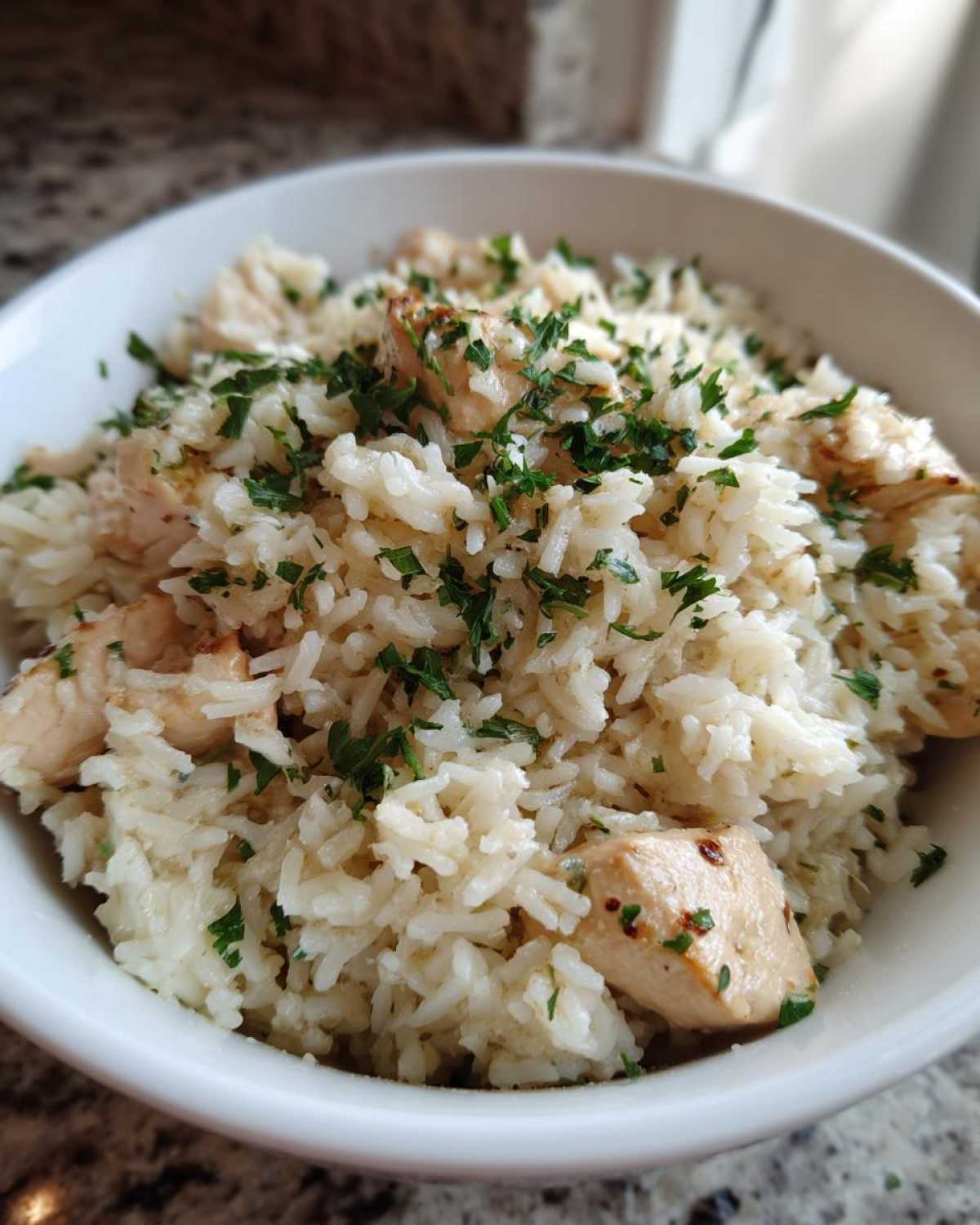 Close-up of Garlic Butter Chicken and Rice Dinner served in a white bowl, topped with fresh parsley.