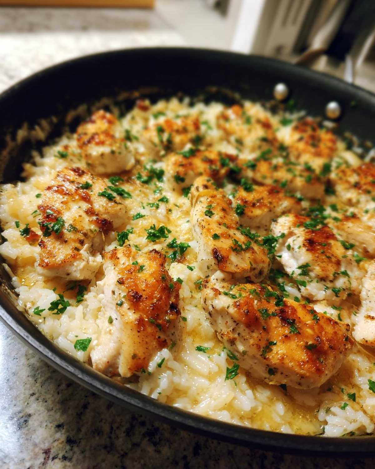 Close-up of golden-brown chicken pieces nestled in creamy Garlic Butter Rice with Chicken Skillet, garnished with parsley.