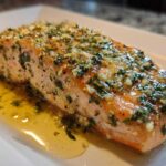 A perfectly cooked fillet of Garlic Butter Salmon with Lemon Herb Sauce glistening with butter and topped with minced garlic and parsley.