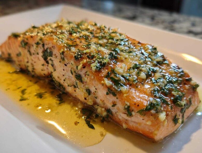 A perfectly cooked fillet of Garlic Butter Salmon with Lemon Herb Sauce glistening with butter and topped with minced garlic and parsley.