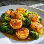 Plump shrimp coated in garlic butter seasoning served with bright green broccoli florets in a white bowl.