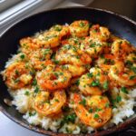 Close-up of juicy Garlic Butter Shrimp and Rice Easy Recipe topped with fresh parsley in a dark skillet.