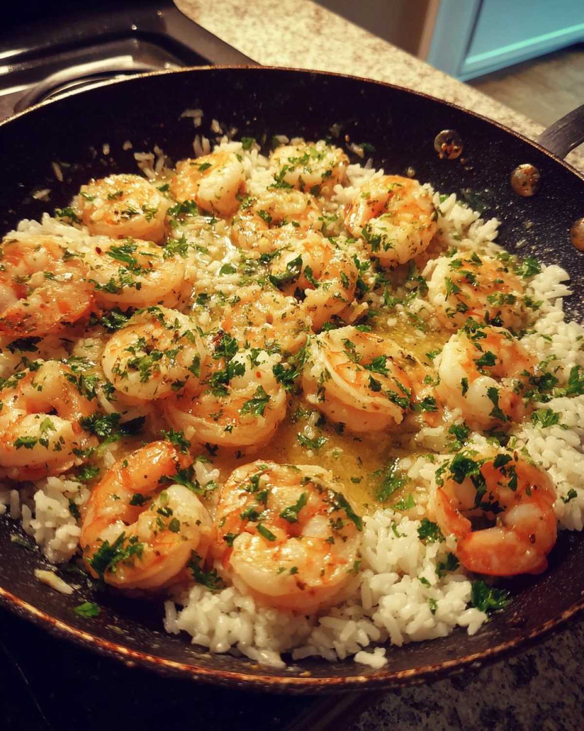 Close-up of plump shrimp cooked in garlic butter sauce served over white rice in a dark skillet, garnished with parsley for the Garlic Butter Shrimp and Rice Easy Recipe.