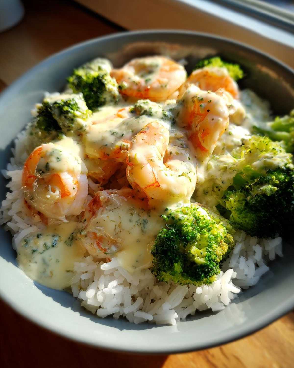 Close-up of a Garlic Butter Shrimp Rice Bowl topped with creamy garlic sauce and bright green broccoli florets.