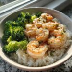 A close-up of a Garlic Butter Shrimp Rice Bowl topped with sautéed shrimp and steamed broccoli florets.