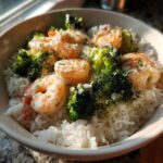 A white bowl filled with white rice, topped with shrimp and broccoli florets drizzled in garlic butter sauce, part of a Garlic Butter Shrimp Rice Bowl.