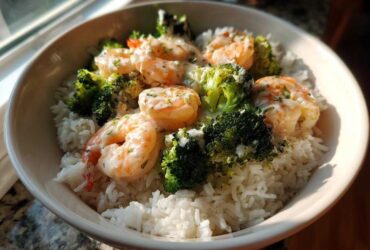 A white bowl filled with white rice, topped with shrimp and broccoli florets drizzled in garlic butter sauce, part of a Garlic Butter Shrimp Rice Bowl.