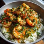 Close-up of a Garlic Butter Shrimp Rice Bowl topped with vibrant green fresh herbs and glistening sauce.
