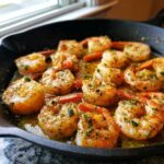 Close-up of plump shrimp cooking in a cast iron skillet with rich garlic butter and lemon sauce.