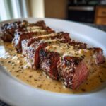 Slices of perfectly cooked Garlic Butter Steak with Creamy Sauce, resting in a pool of the sauce on a white platter.