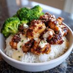Close-up of a Honey Garlic Chicken Bowl with crispy chicken pieces, white rice, steamed broccoli, and drizzled with a creamy sauce.