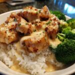 Close-up of a Honey Garlic Chicken Bowl featuring glazed chicken pieces smothered in creamy sauce over white rice and bright green broccoli florets.