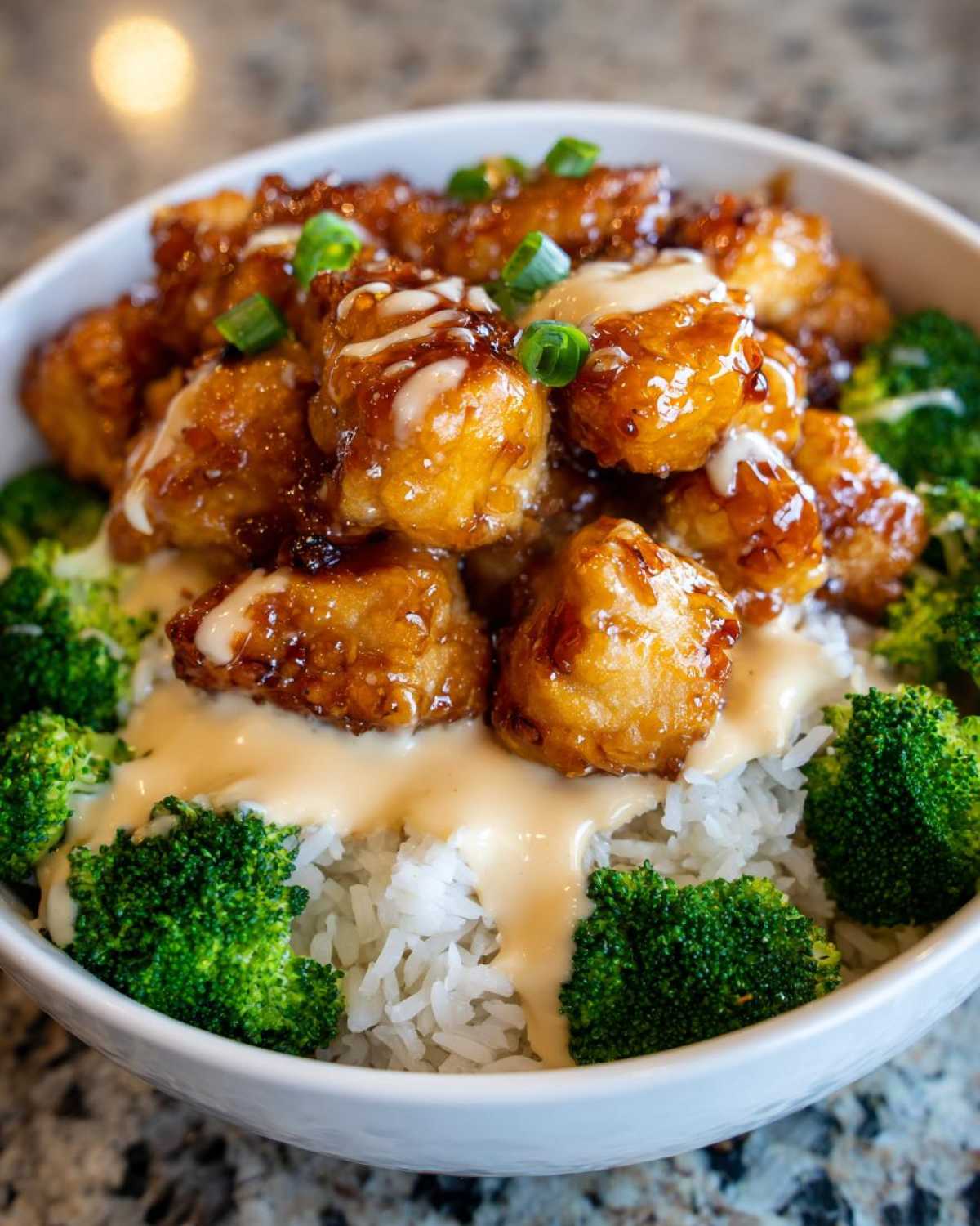Close-up of a Honey Garlic Chicken Bowl featuring glazed chicken pieces over rice, broccoli, and drizzled with creamy sauce.