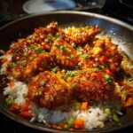 Close-up of glazed Honey Garlic Chicken Skillet with Rice, topped with scallions and peppers in a dark skillet.