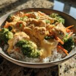 A close-up of a Honey Mustard Chicken Bowl featuring chicken pieces, broccoli, carrots, and rice topped with a creamy sauce and sesame seeds.