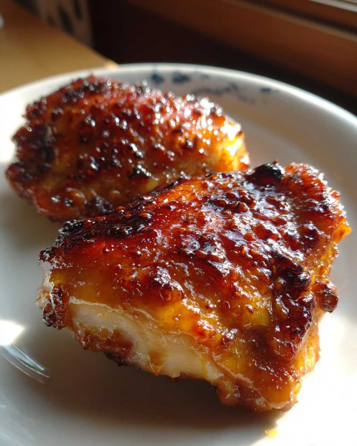 Close-up of two glistening, caramelized Honey Mustard Chicken Thighs Oven Roasted pieces on a white plate.