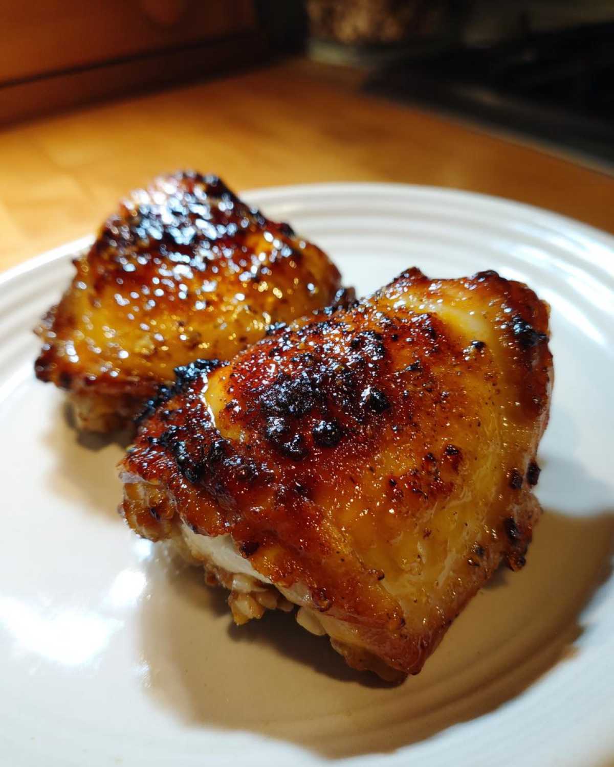 Two perfectly cooked Honey Mustard Chicken Thighs Oven Roasted pieces with a shiny, caramelized glaze on a white plate.