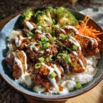 Close-up of a Honey Soy Chicken Bowl featuring glazed chicken pieces over white rice, drizzled with white sauce and green onions.