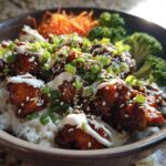 Close-up of a Honey Soy Chicken Bowl featuring glazed chicken pieces over white rice, topped with white sauce, sesame seeds, and green onions.