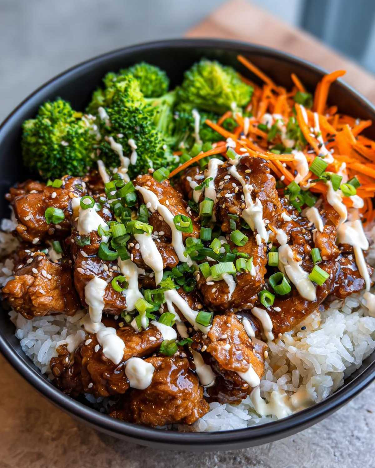 Close-up of a Honey Soy Chicken Bowl featuring glazed chicken pieces over rice, topped with white sauce, green onions, and sesame seeds.