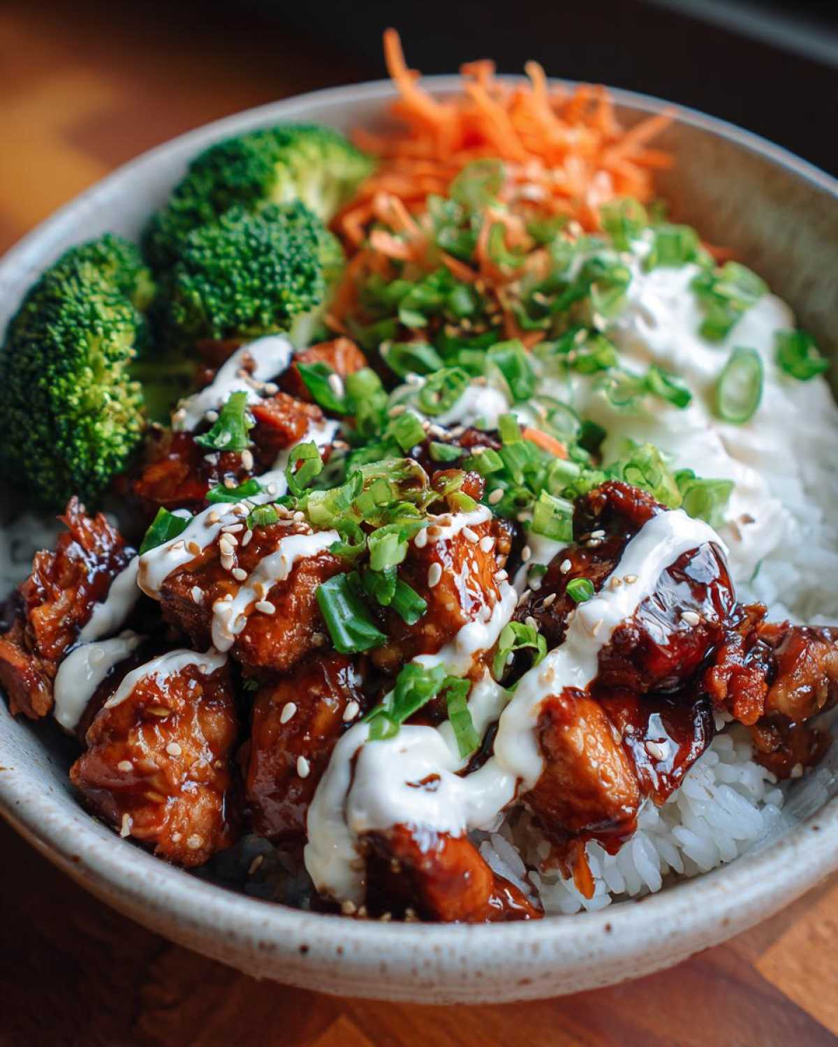 A close-up of a Honey Soy Chicken Bowl featuring glazed chicken pieces over rice, topped with garlic sauce, green onions, and sesame seeds.