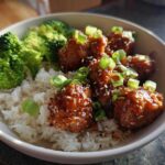 A close-up of a Honey Soy Chicken Bowl featuring glazed chicken pieces, white rice, and steamed broccoli, topped with green onions.