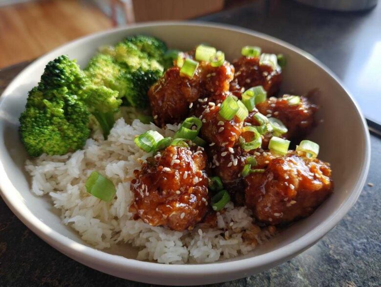 A close-up of a Honey Soy Chicken Bowl featuring glazed chicken pieces, white rice, and steamed broccoli, topped with green onions.
