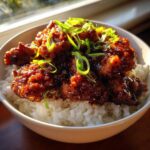 Close-up of Honey Soy Garlic Chicken pieces coated in a dark, glossy sauce served over white rice and topped with green onions.
