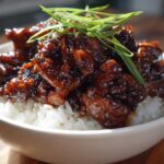 Close-up of Honey Soy Garlic Chicken with a thick, dark glaze served over fluffy white rice and garnished with green onions.
