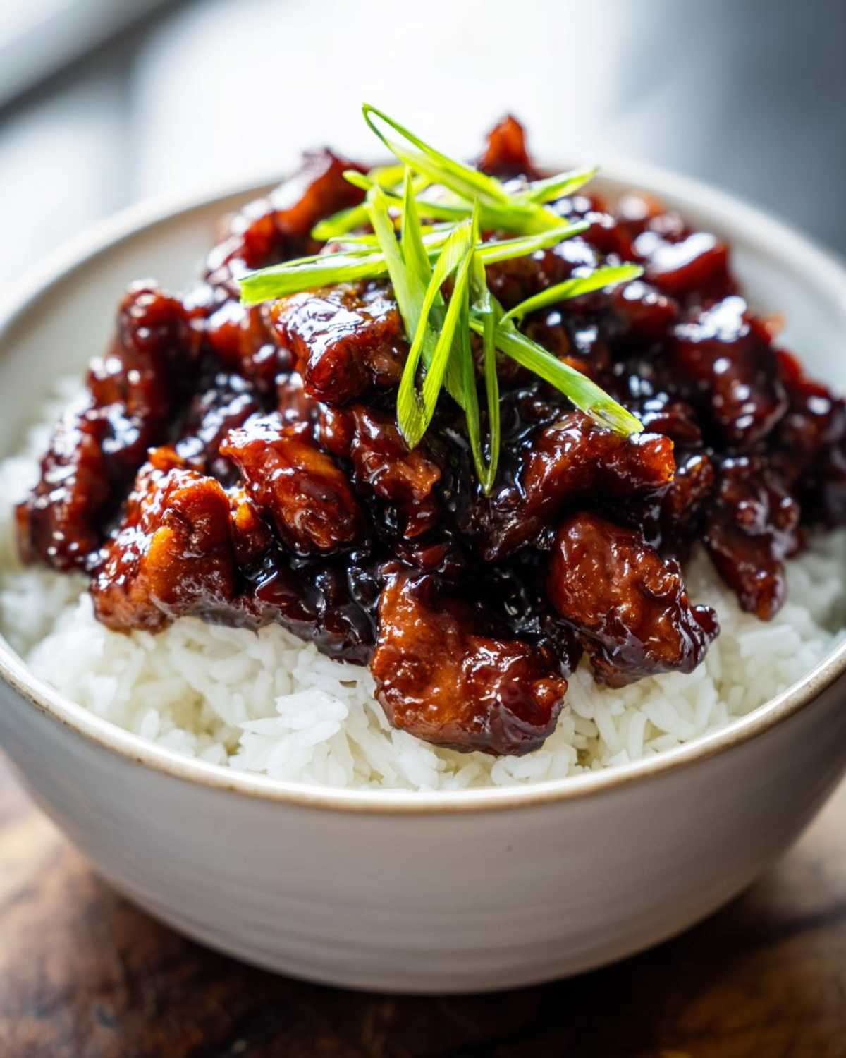 Close-up of Honey Soy Garlic Chicken pieces coated in a dark, glossy sauce served over fluffy white rice, garnished with green onions.
