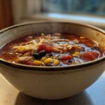 Close-up of a steaming bowl filled with rich Instant Pot Chicken Tortilla Soup, showing shredded chicken, corn, black beans, and tomatoes.