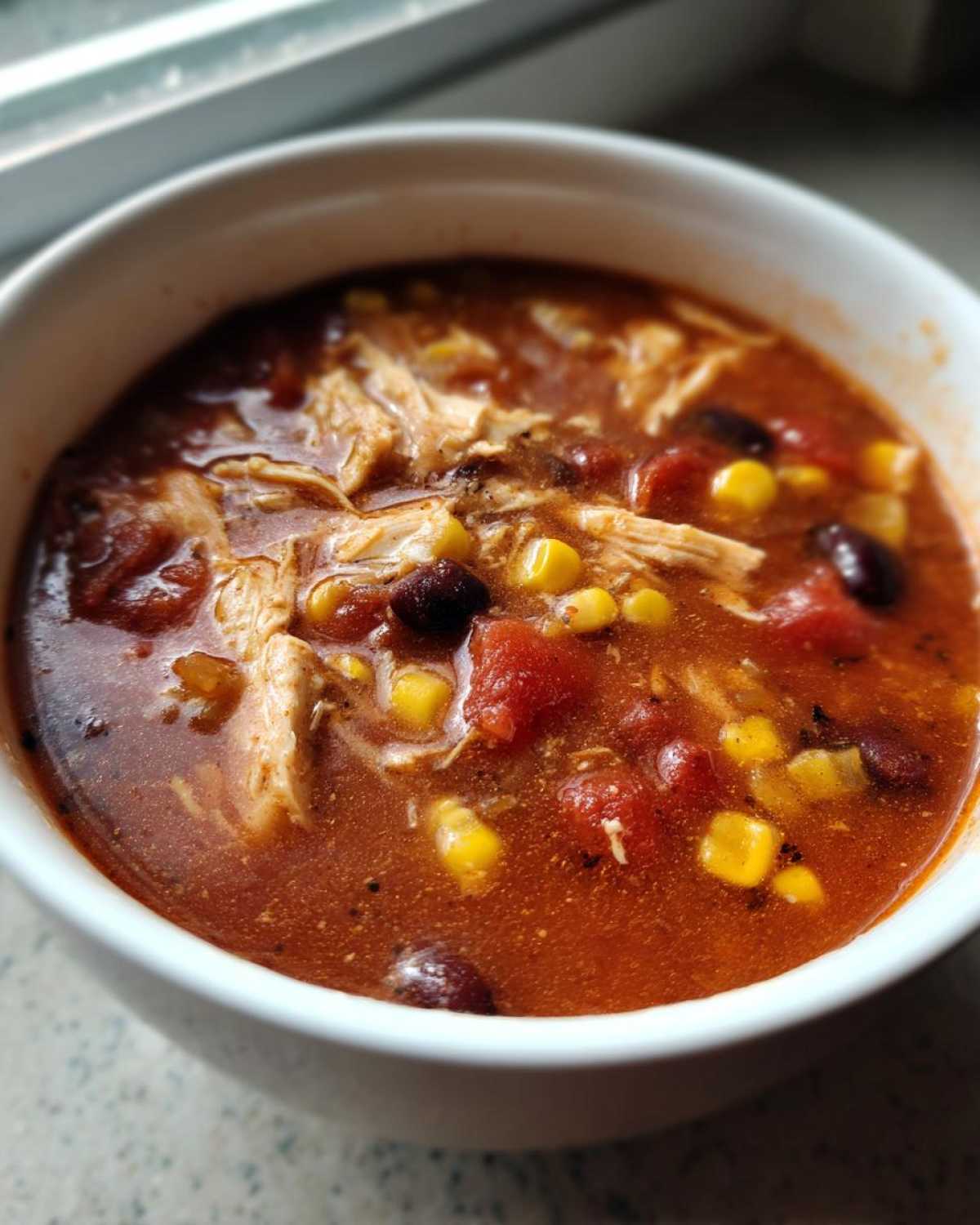 Close-up of a white bowl filled with rich, red Instant Pot Chicken Tortilla Soup featuring shredded chicken, black beans, corn, and diced tomatoes.
