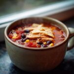 Close-up of hot Instant Pot Chicken Tortilla Soup topped with shredded chicken, black beans, corn, and tortilla chips.