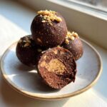 Close-up of Keto Chocolate Peanut Butter Fat Bombs, one cut open revealing a peanut butter center, topped with chopped nuts.