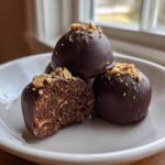 Close-up of chocolate-covered Keto Chocolate Peanut Butter Fat Bombs, one cut open to show the texture, topped with chopped peanuts.