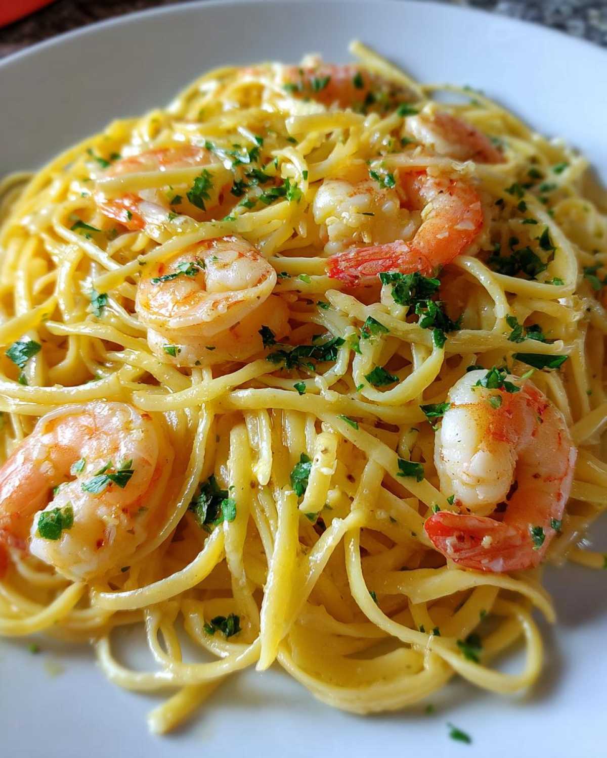 A close-up of a serving of Lemon Butter Shrimp Pasta Ready in 20 Minutes, topped with bright pink shrimp and fresh parsley.