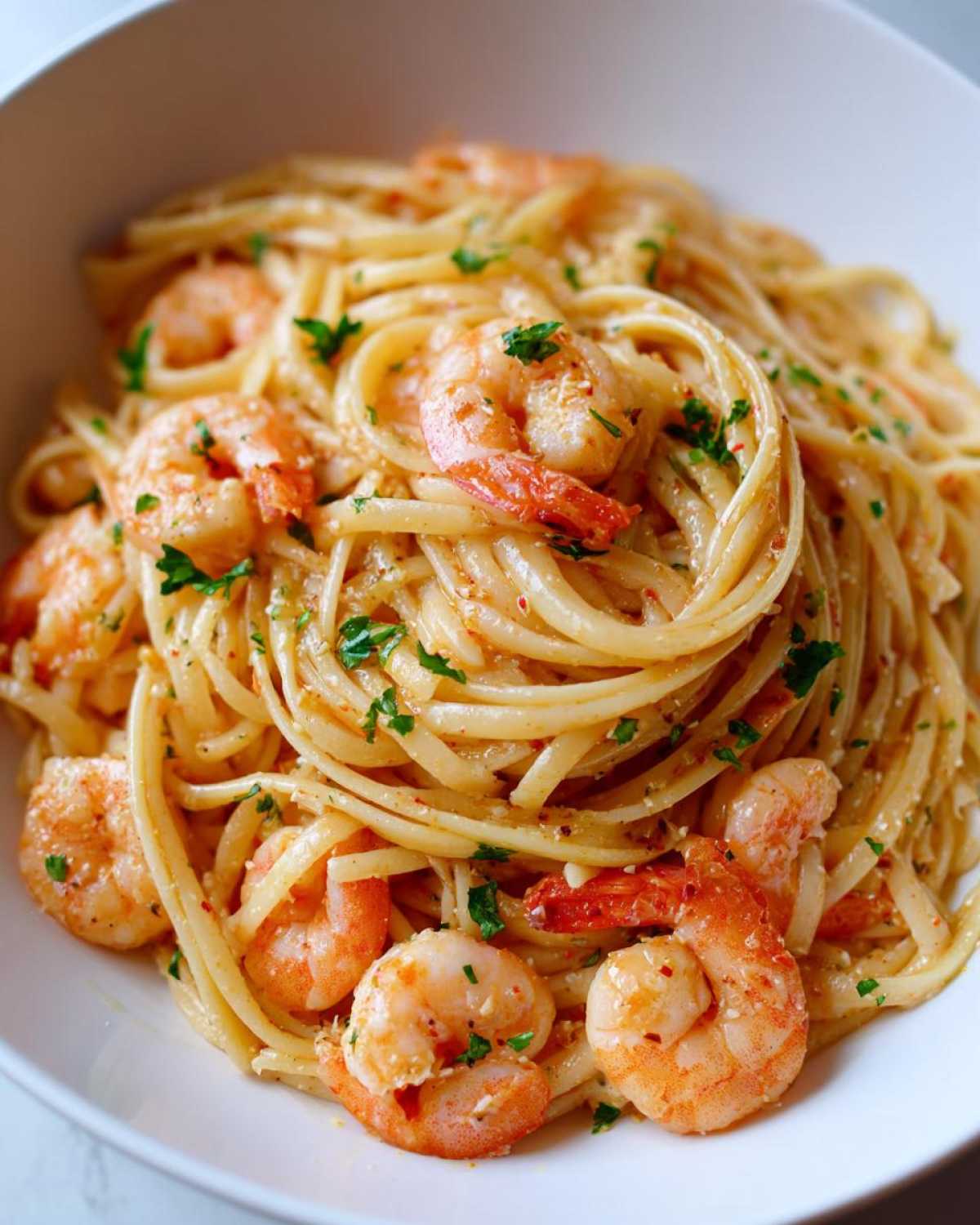A close-up of a white bowl filled with Lemon Butter Shrimp Pasta Ready in 20 Minutes, garnished with parsley.