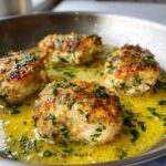 Four golden-brown chicken pieces simmering in bright yellow lemon garlic butter sauce, topped with fresh parsley.