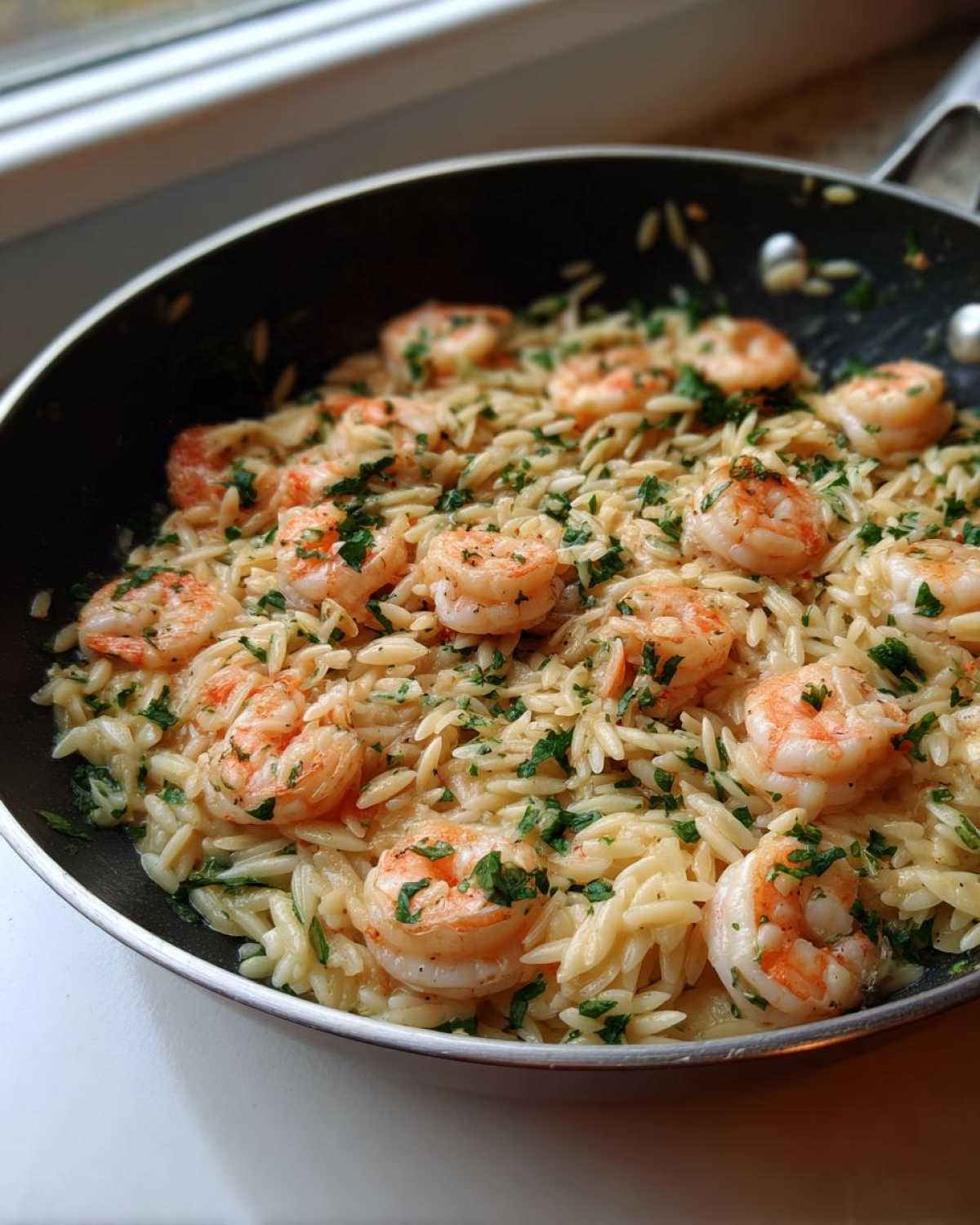 Close-up of Lemon Garlic Shrimp Orzo One Pan Dinner cooked in a black skillet, garnished with parsley.
