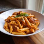 Close-up of One Pot Creamy Tomato Pasta with Chicken served in a white bowl, garnished with basil.