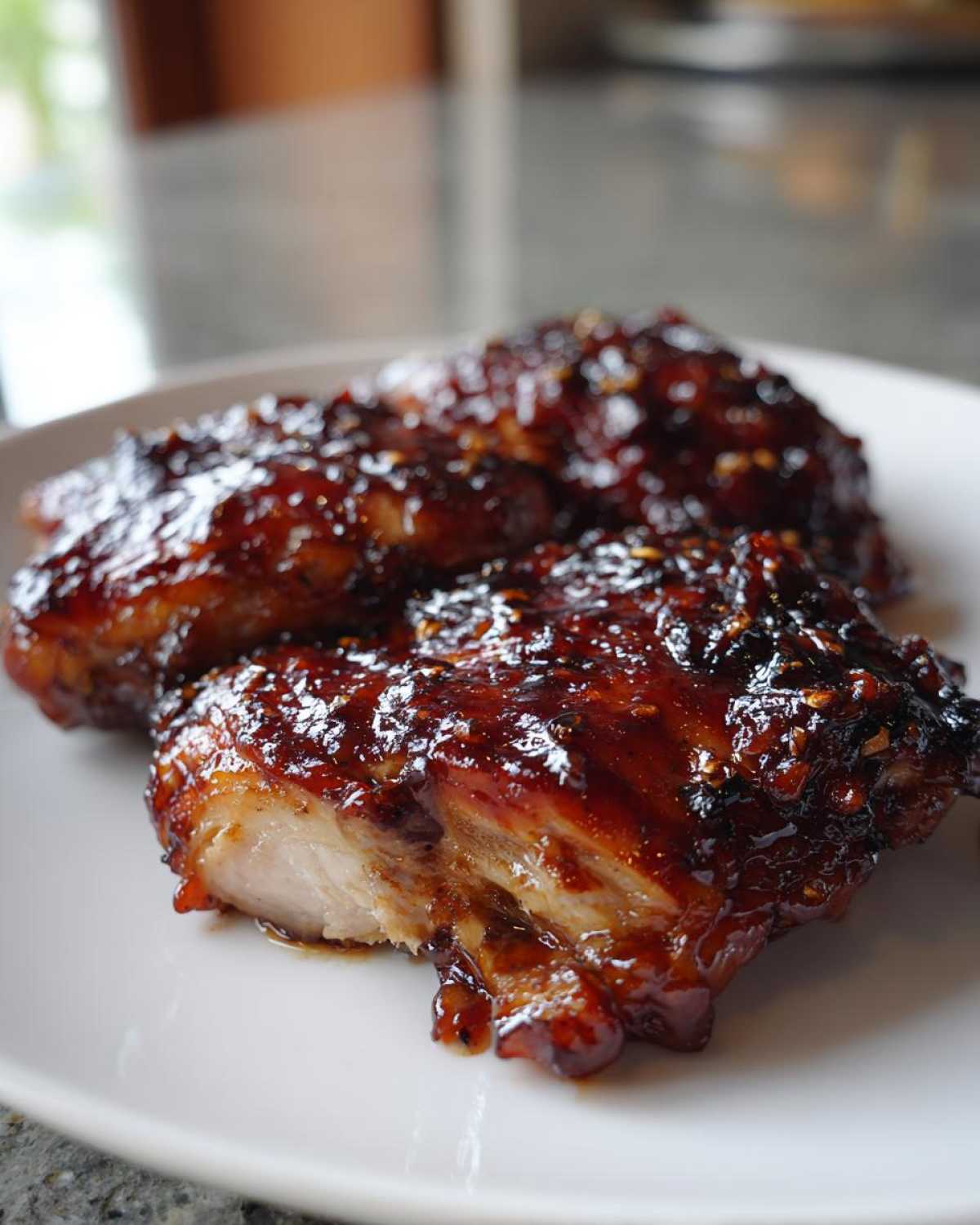 Two pieces of juicy Sticky BBQ Chicken Thighs with Honey Glaze, showing the thick, dark, caramelized sauce.
