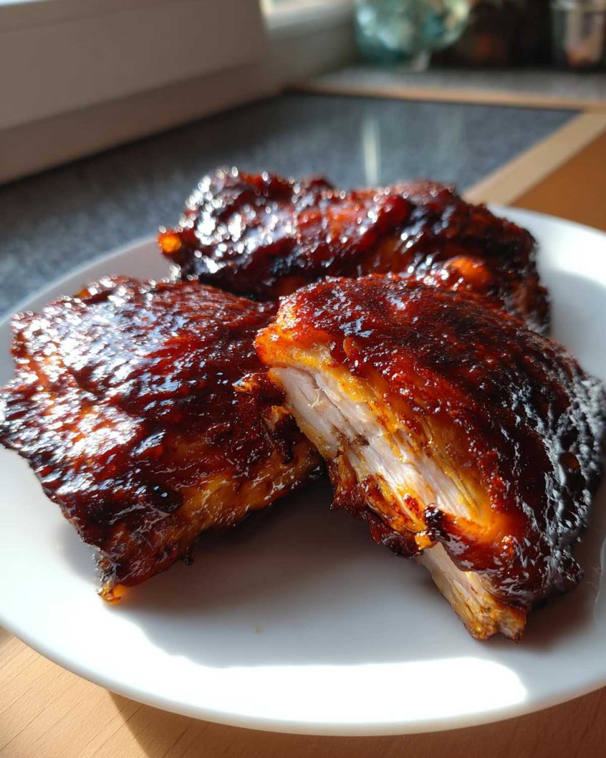 Close-up of three Sticky BBQ Chicken Thighs with Honey Glaze, one cut open to show juicy white meat.