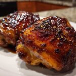 Two perfectly glazed Sticky Honey Soy Chicken Thighs with Garlic resting on a white plate.