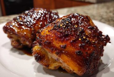 Two perfectly glazed Sticky Honey Soy Chicken Thighs with Garlic resting on a white plate.