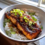 Close-up of a perfectly cooked Sticky Honey Soy Salmon fillet served over white rice and garnished with sesame seeds and green onions.