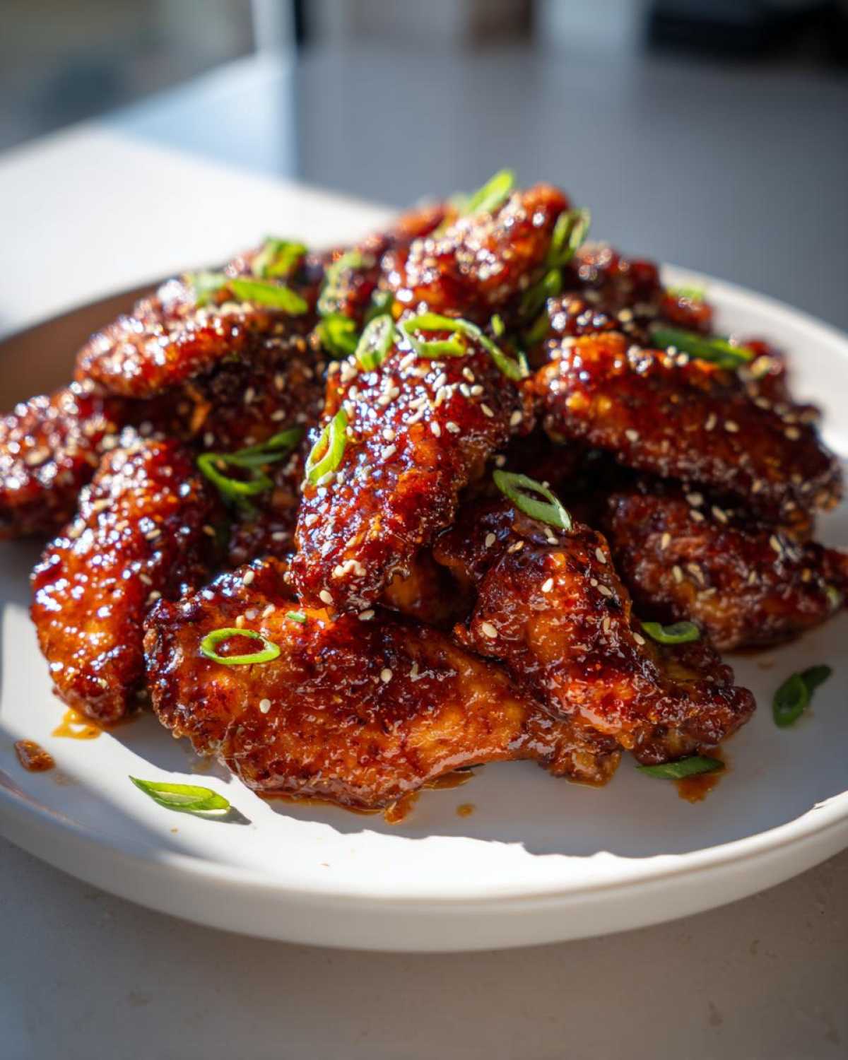 A pile of Sticky Orange Chicken Wings with Honey Glaze, glistening and topped with sesame seeds and sliced green onions.