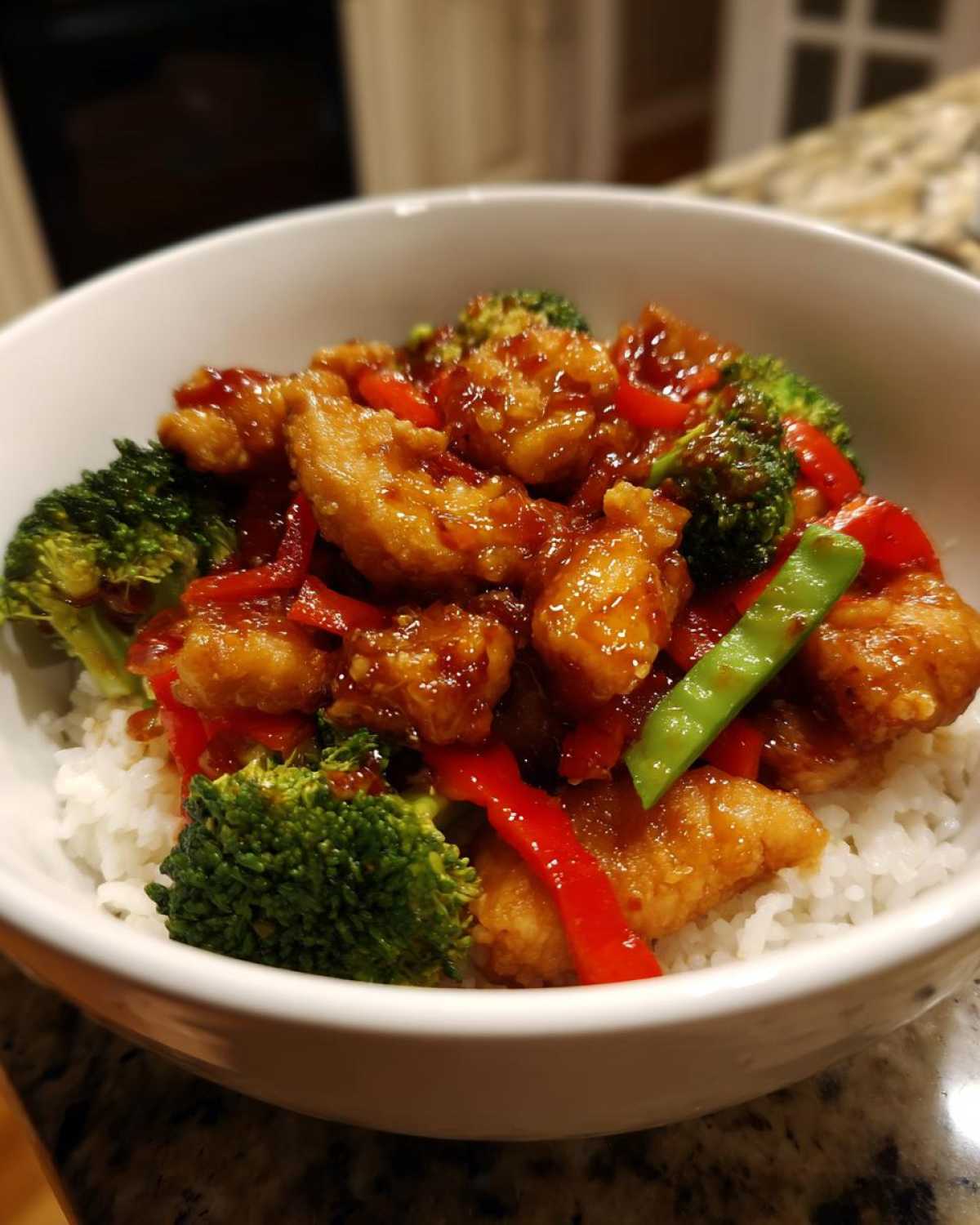 Close-up of a Sticky Sweet Chili Chicken Bowl with rice, broccoli, and red peppers coated in a glossy sauce.