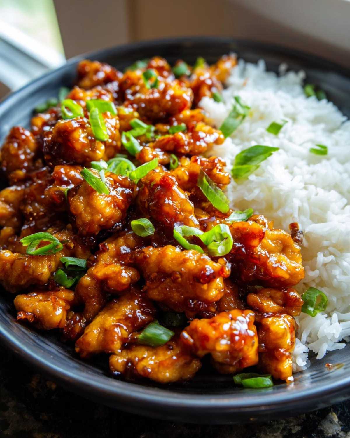 Close-up of Sticky Sweet Chili Chicken Skillet pieces coated in glaze next to fluffy white rice, garnished with green onions.