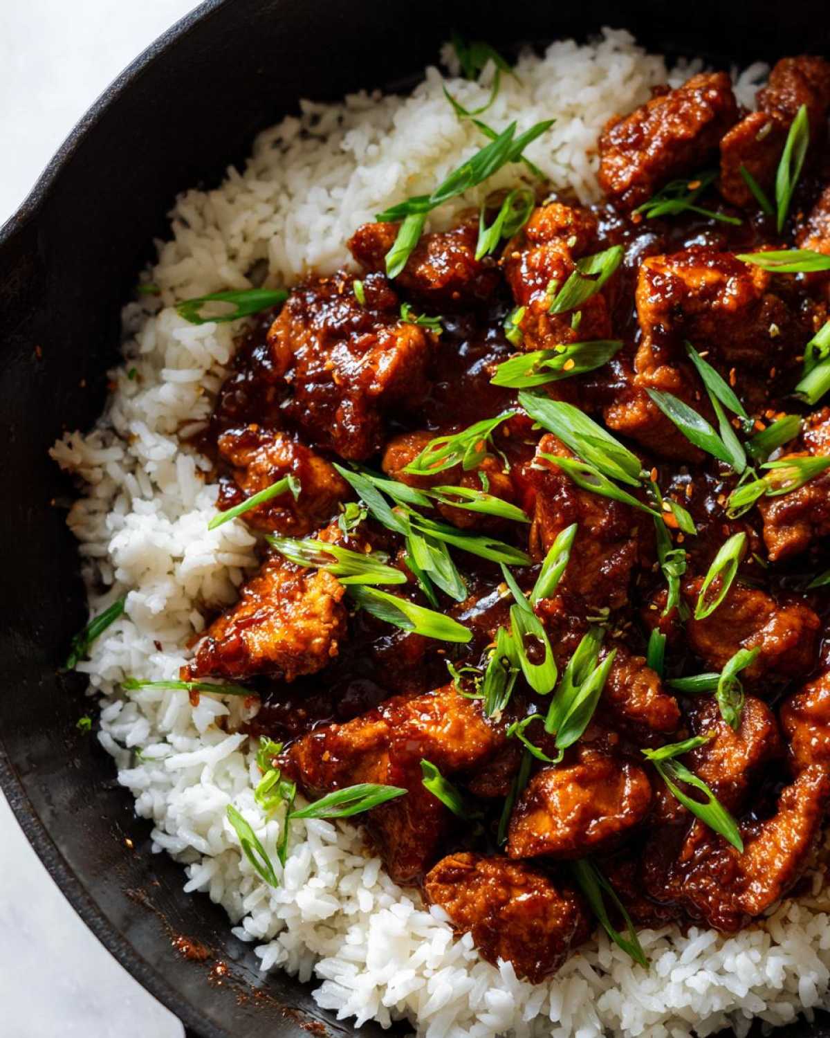 Close-up of Sticky Sweet Chili Chicken Skillet served over white rice and garnished with fresh green onions.